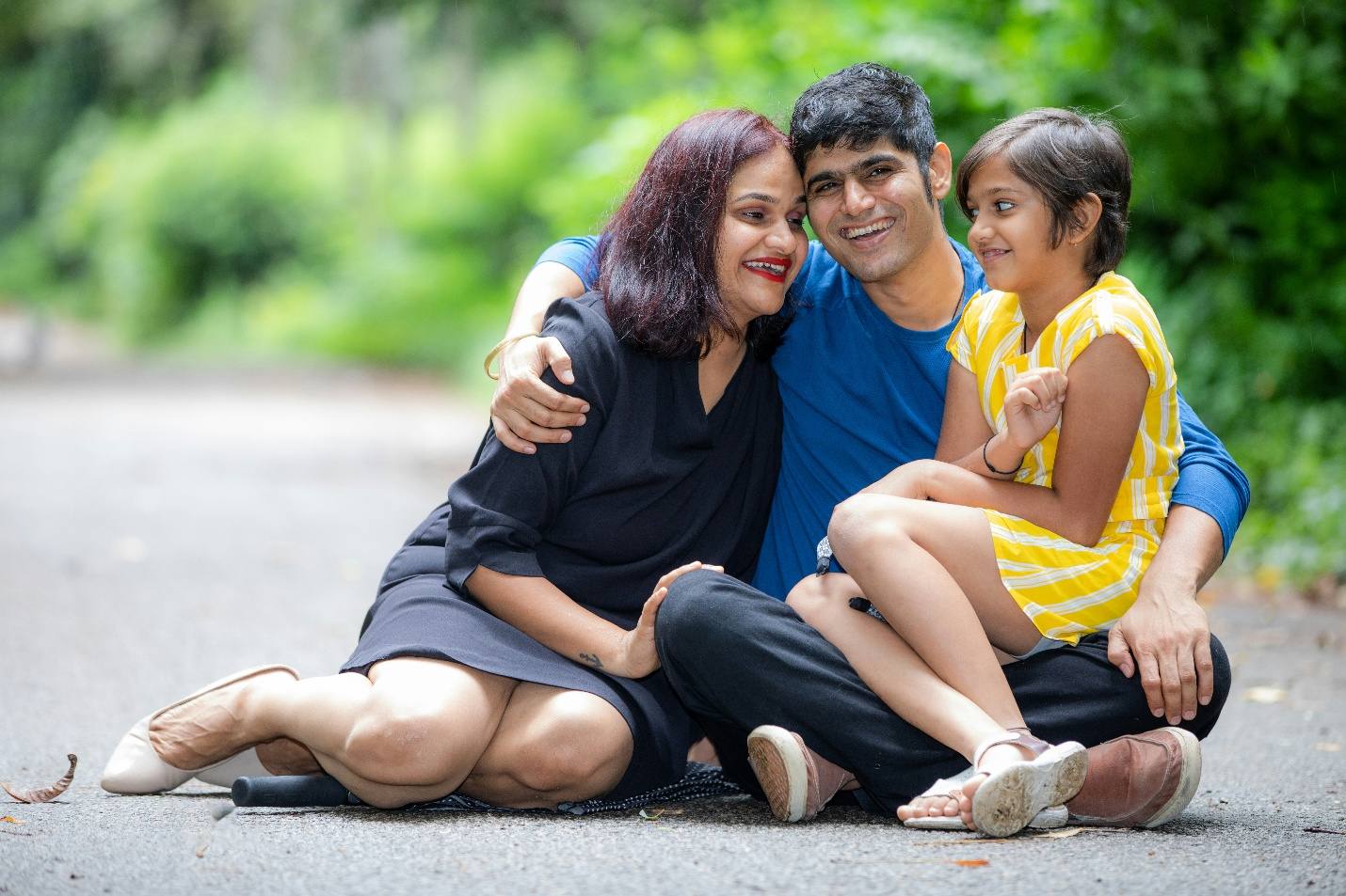 A family of three sitting close together outdoors, smiling.
