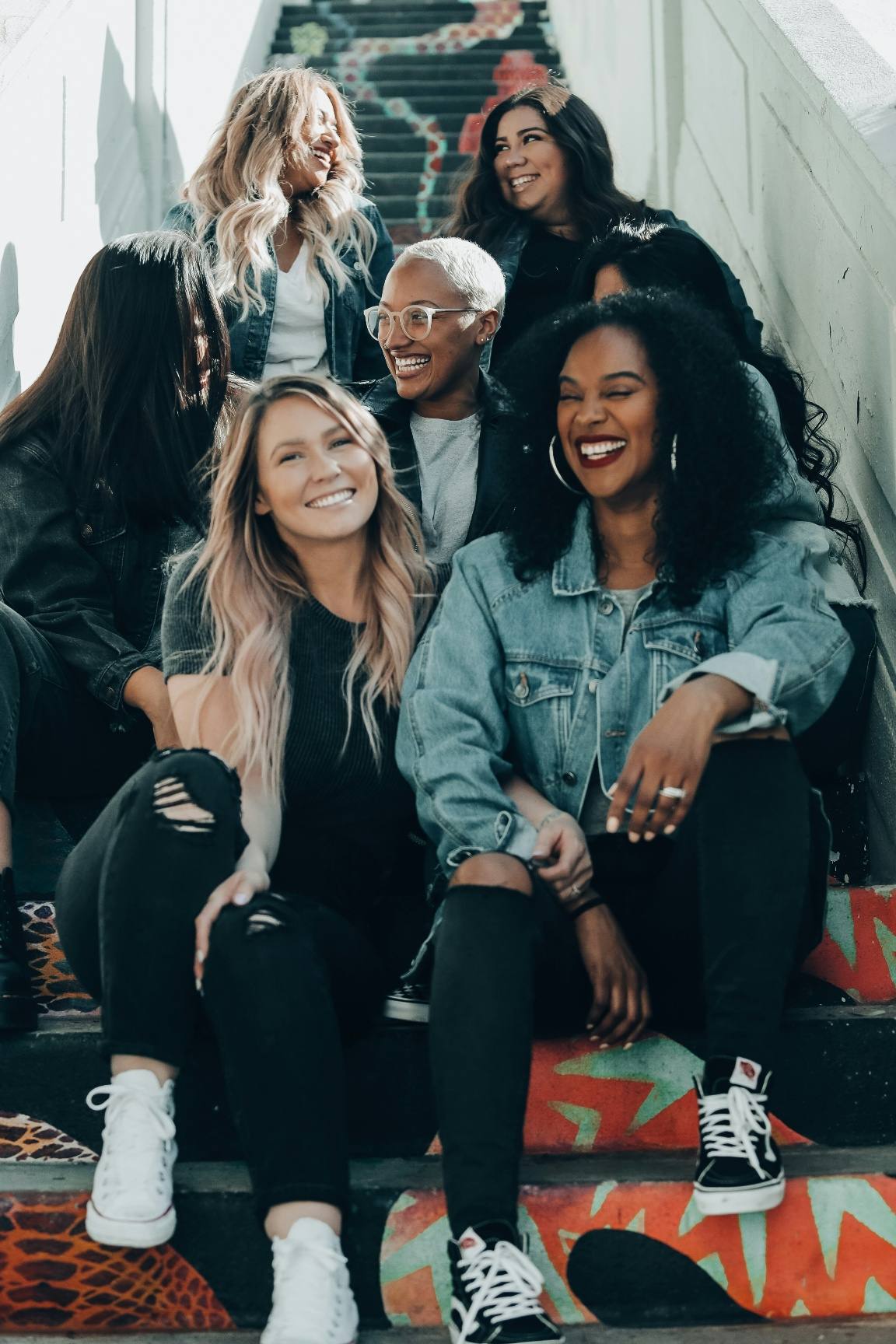 A diverse group of young women laughing together, sitting on colourfully painted steps.