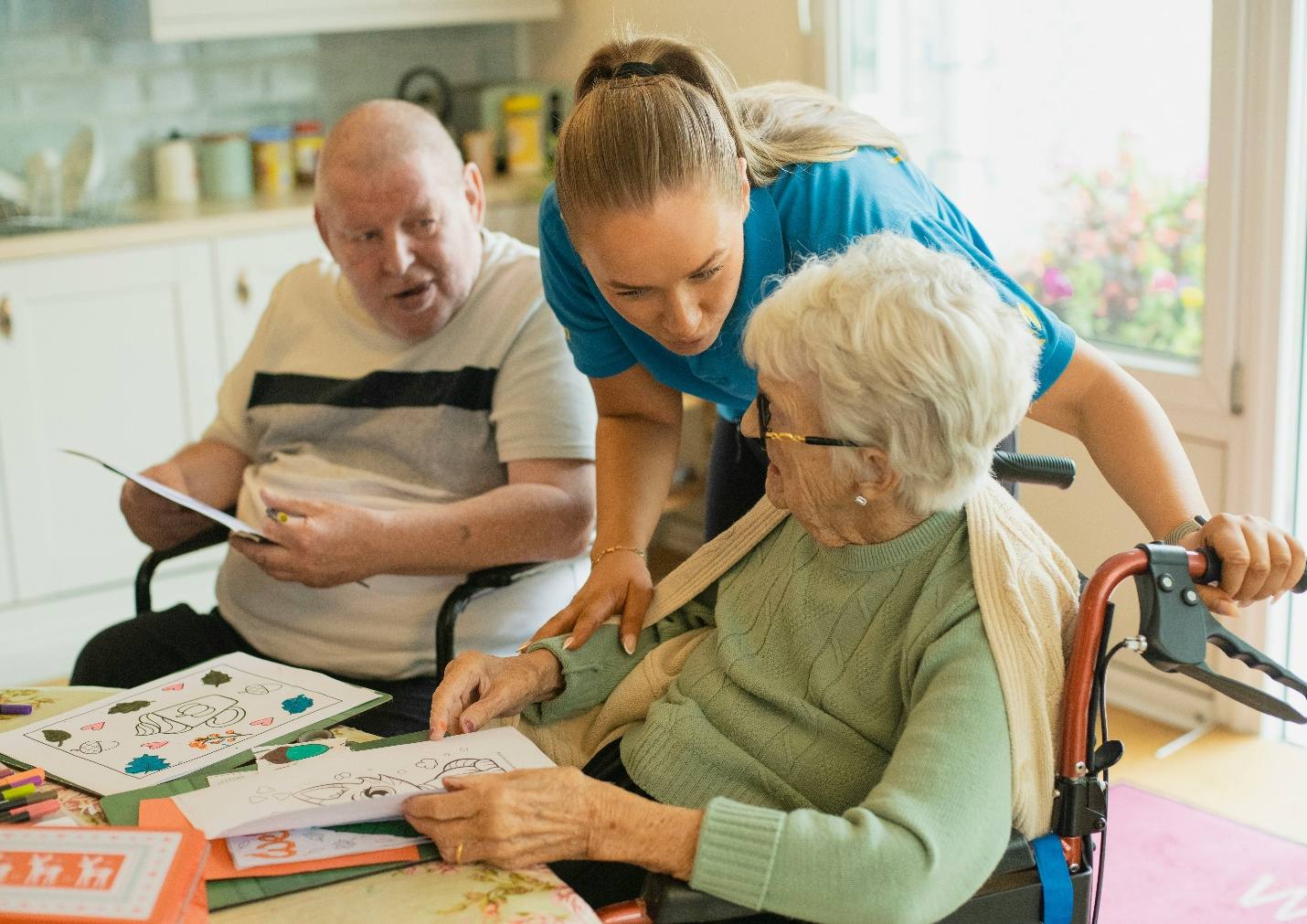 A support worker helping an older couple at a kitchen table.