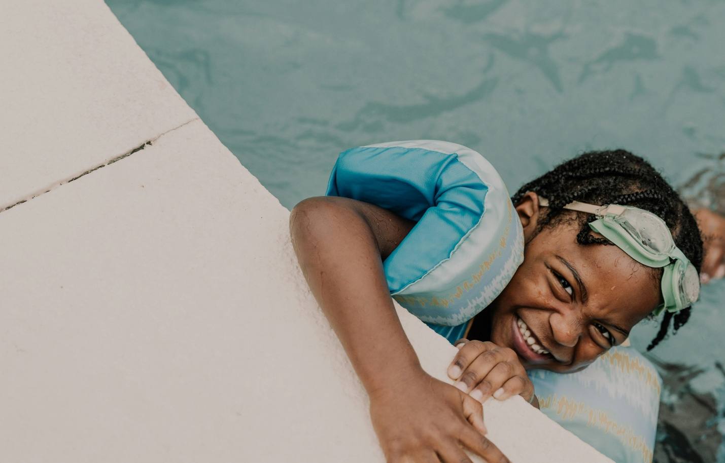A child laughing while playing in a swimming pool, wearing arm floats.